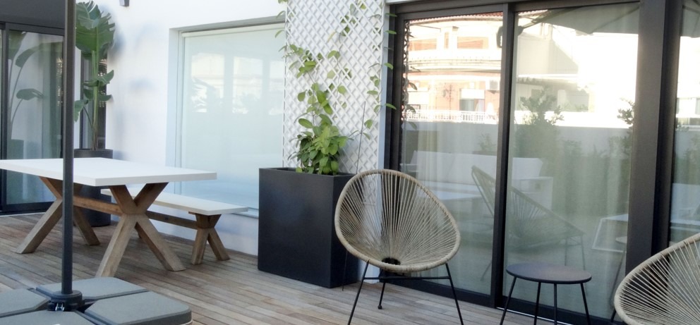 Terraza bonita y moderna con una mesa blanca con patas de madera y unas sillas de diseño. Espacio diseñado por Integra Estudio de Interiores.